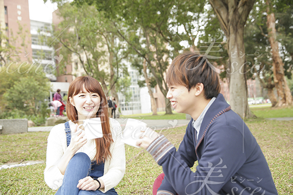 大学生の男性と笑顔でキャンパスの芝生に座る女性