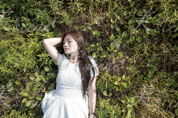 草むらに寝転がる白い服の女性