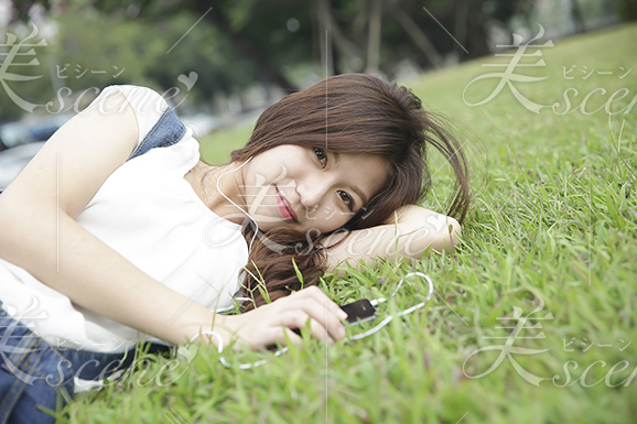 芝生に寝そべって音楽を聴く女性