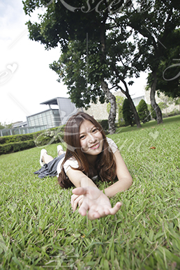 芝生に寝そべりながら手を差し伸べる女性