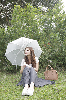 傘をさしながら芝生に座る女性