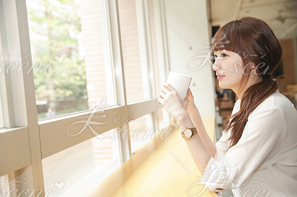 カフェで飲み物を飲みながら窓の外の風景を眺める女性