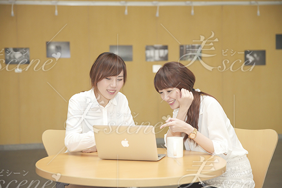 カフェでノートパソコンを開き、一緒に見ながら笑う女性二人
