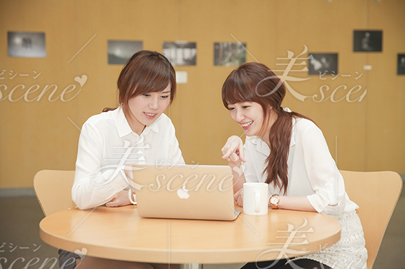 ノートパソコンの画面を指差し、一緒に見ながら笑う女性二人組