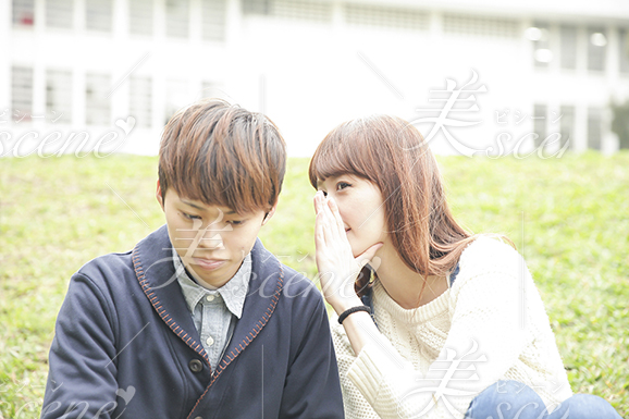 大学生の男性にキャンパス内の芝生に座りながら内諸話する女性