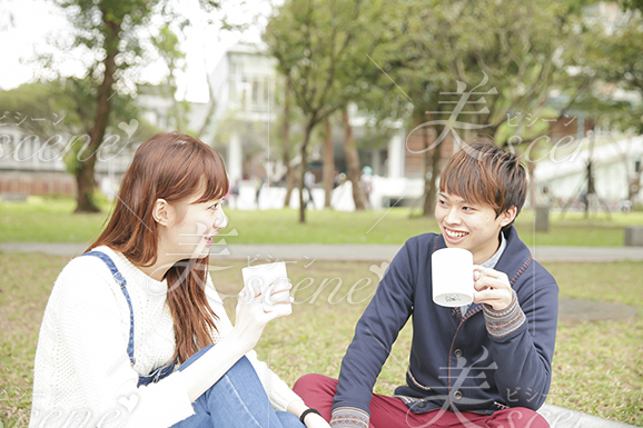 男性と大学のキャンパス内の芝生に座りながら飲み物を飲む女性