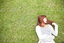 芝生に寝転がり遠くを見る女性