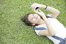 芝生に寝そべってスマホをいじる女性