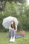 傘をさしながら芝生に座る女性