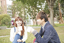 大学生の男性と笑顔でキャンパスの芝生に座る女性